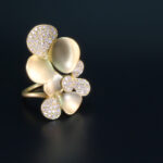 close up photo of gold and diamond ring with clover design on black background