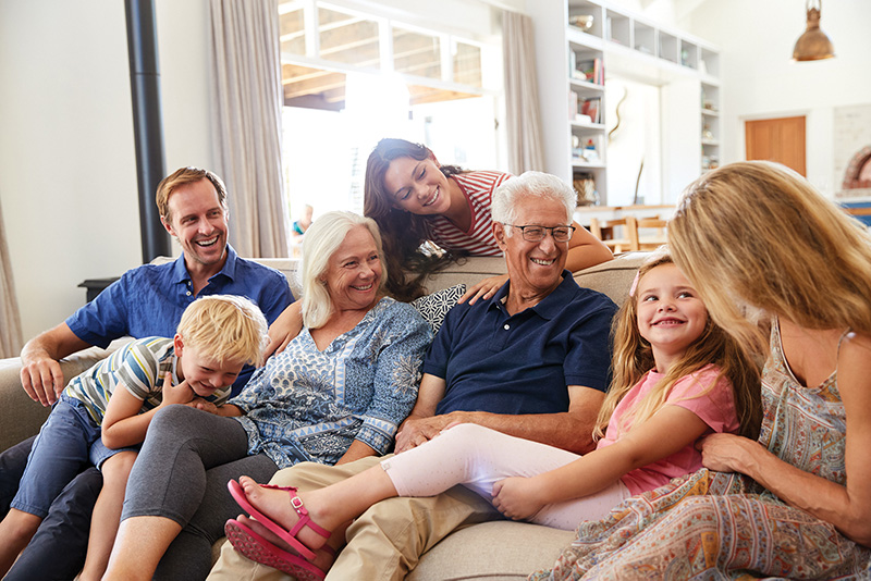 family members of multiple generations sitting on and gathered around a couch in a bright sunny family room