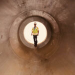 construction worker viewed at end of large drainage pipe