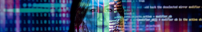 a woman is in a dark room with multicolored data and computer code projected across her upper body and the walls behind her