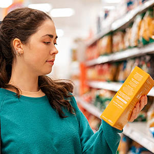 Portrait of a young Caucasian beautiful woman who reads the ingredients on the product packaging. Shelves with goods in a blur in the background. The concept of buying goods and shopping.